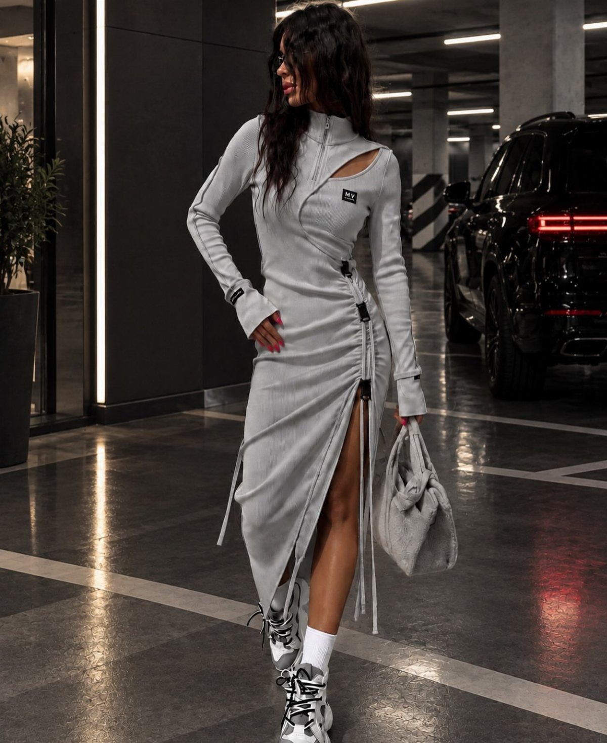 Woman wearing a grey athletic dress and white sneakers in a parking garage.