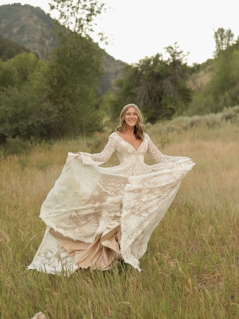 Woman in a long-sleeved lace boho wedding dress smiling in a grassy field.