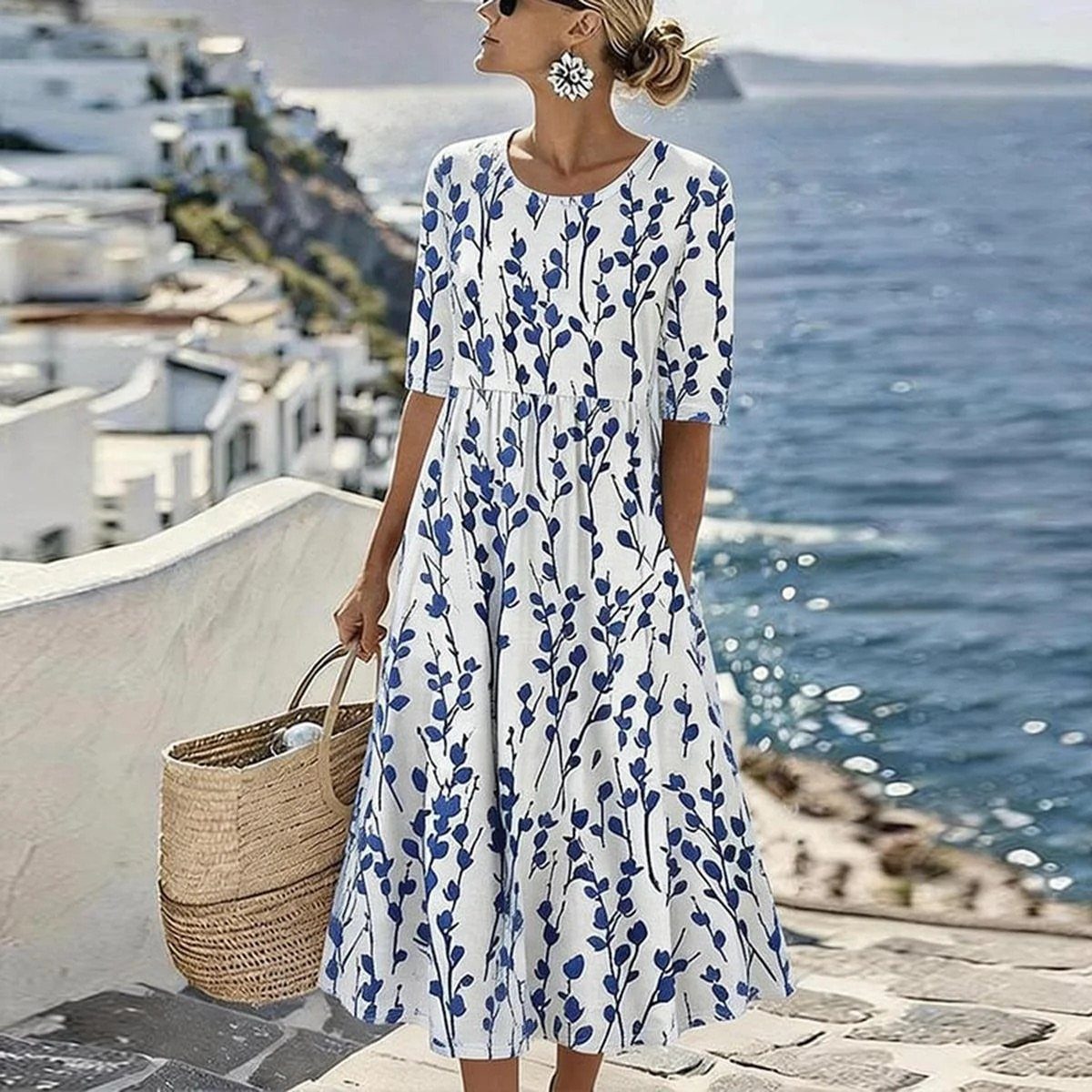 Woman in a white and blue floral summer dress holding a straw bag seaside.