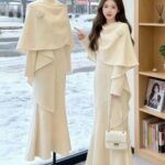 Woman and mannequin wearing cream winter dresses with capelets and floral details.