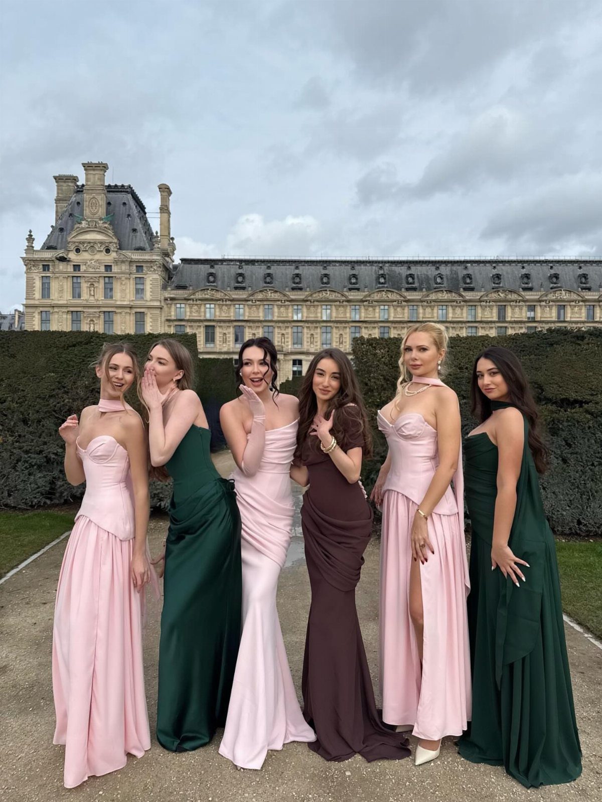 Six women wearing elegant pink and green maxi dresses posing before a French chateau.