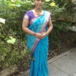 Woman wearing a bright blue saree with purple accents posing in a green garden