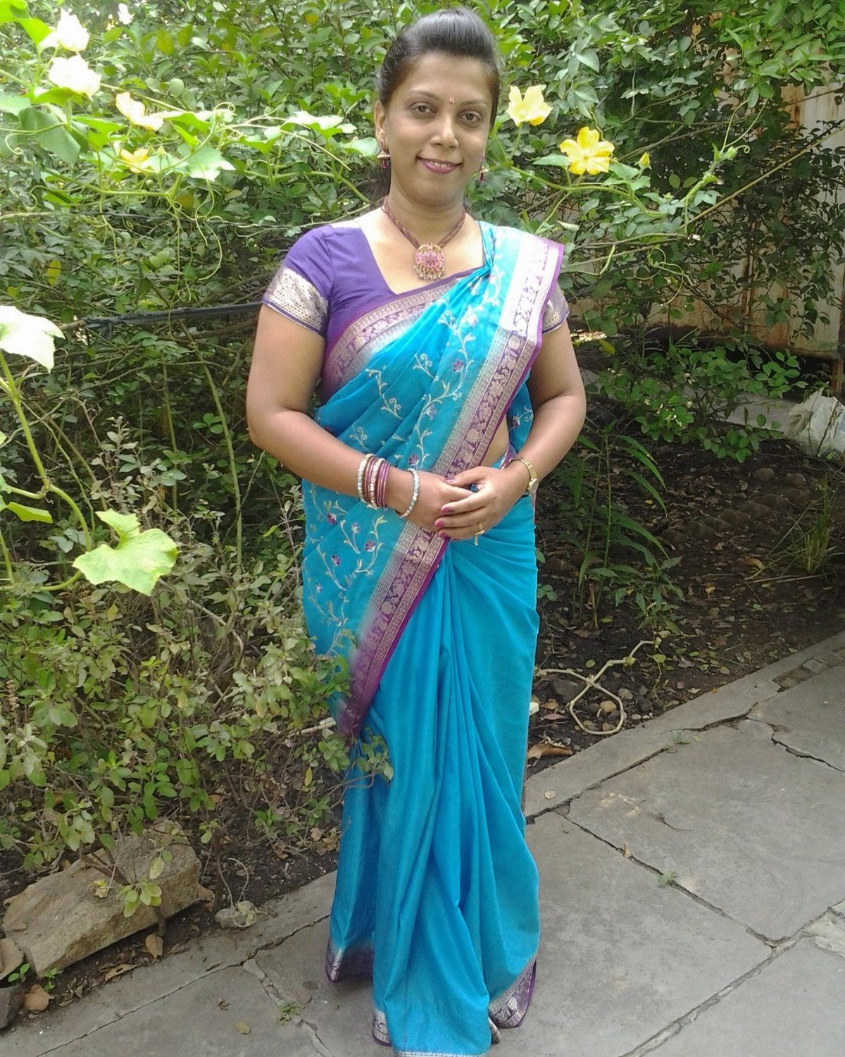 Woman wearing a bright blue saree with purple accents posing in a green garden