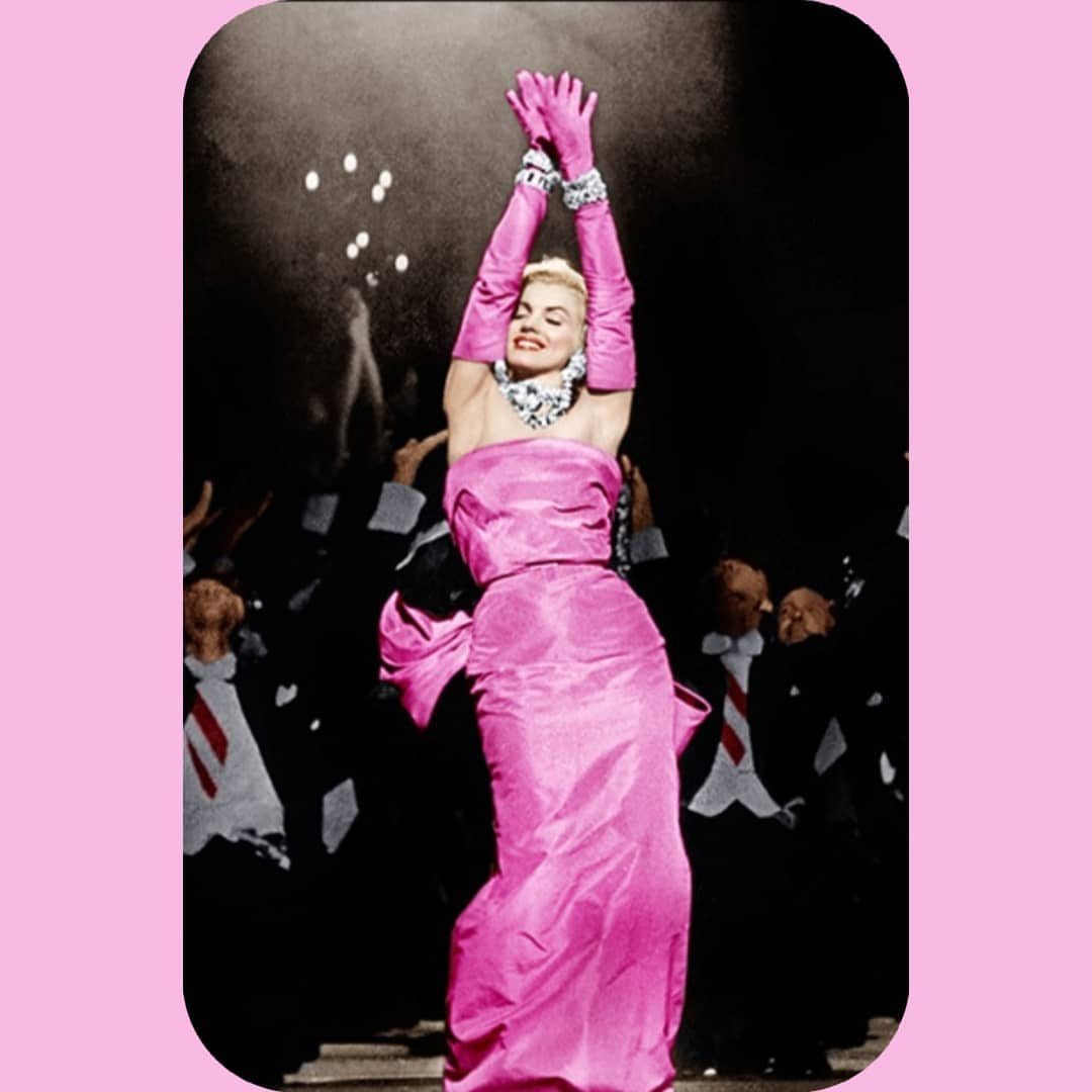 Woman in a strapless pink satin gown and matching opera gloves posing with arms raised.