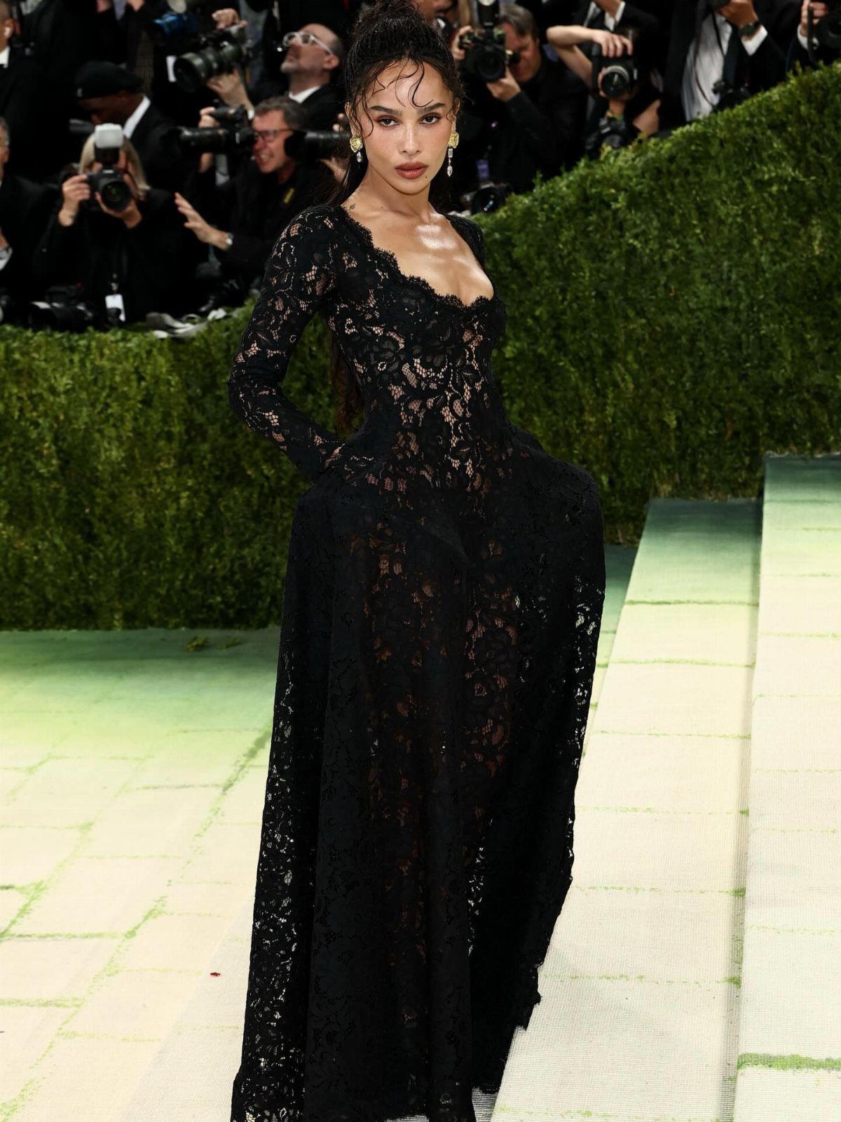 Woman in a long-sleeved black lace gown posing on a red carpet event.