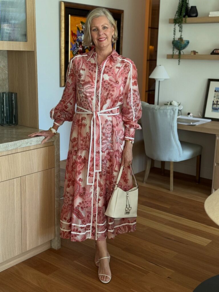 Mature woman wearing a red floral midi casual dress and white sandals indoors.