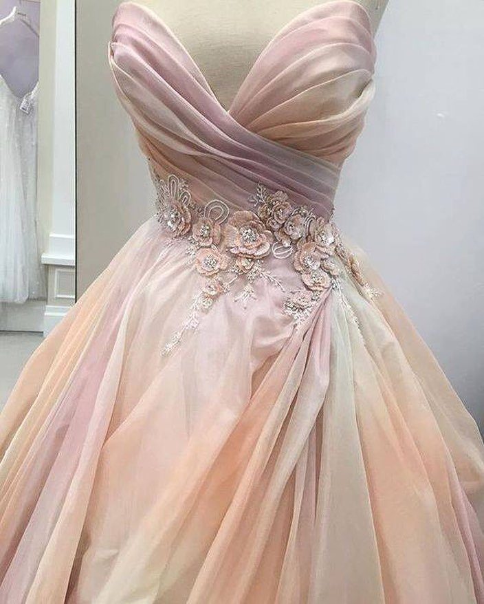 Pink and peach strapless wedding gown with floral lace embellishments on a mannequin