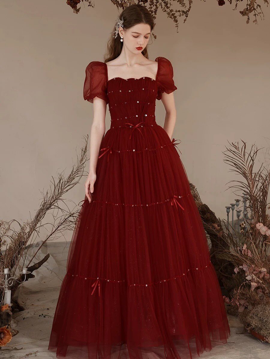 Woman wearing a voluminous deep red tulle prom dress with puffed sleeves and bows.