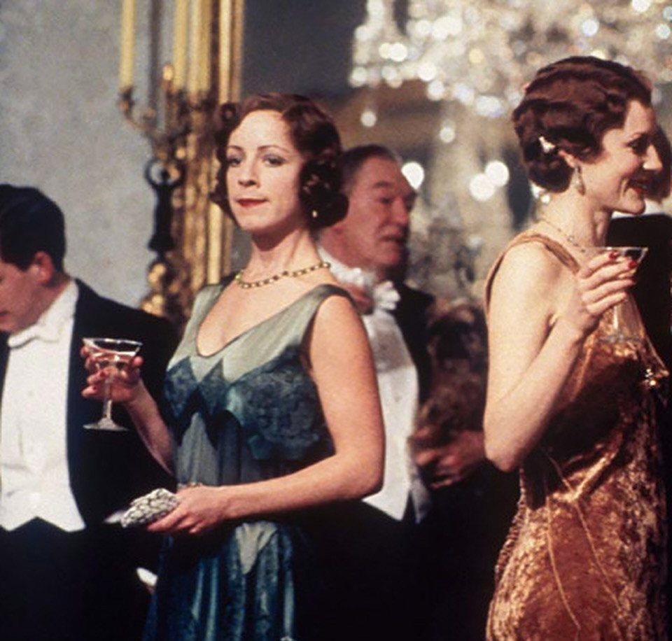 Women in shimmering flapper dresses and men in tuxedos at a 1920s party.