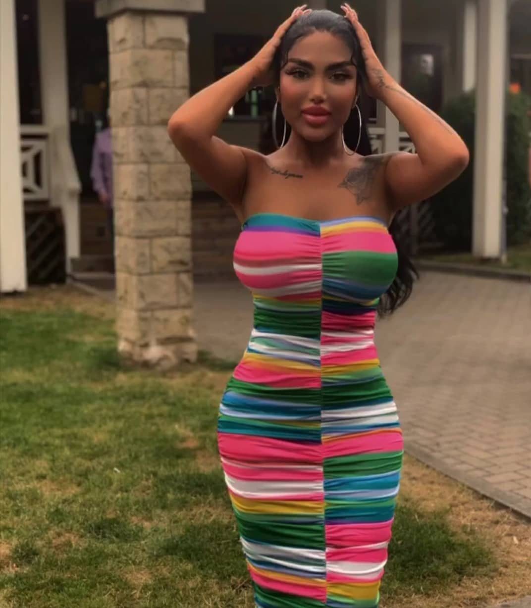 Woman wearing a colorful striped strapless bandeau mini dress posing outdoors on grass.