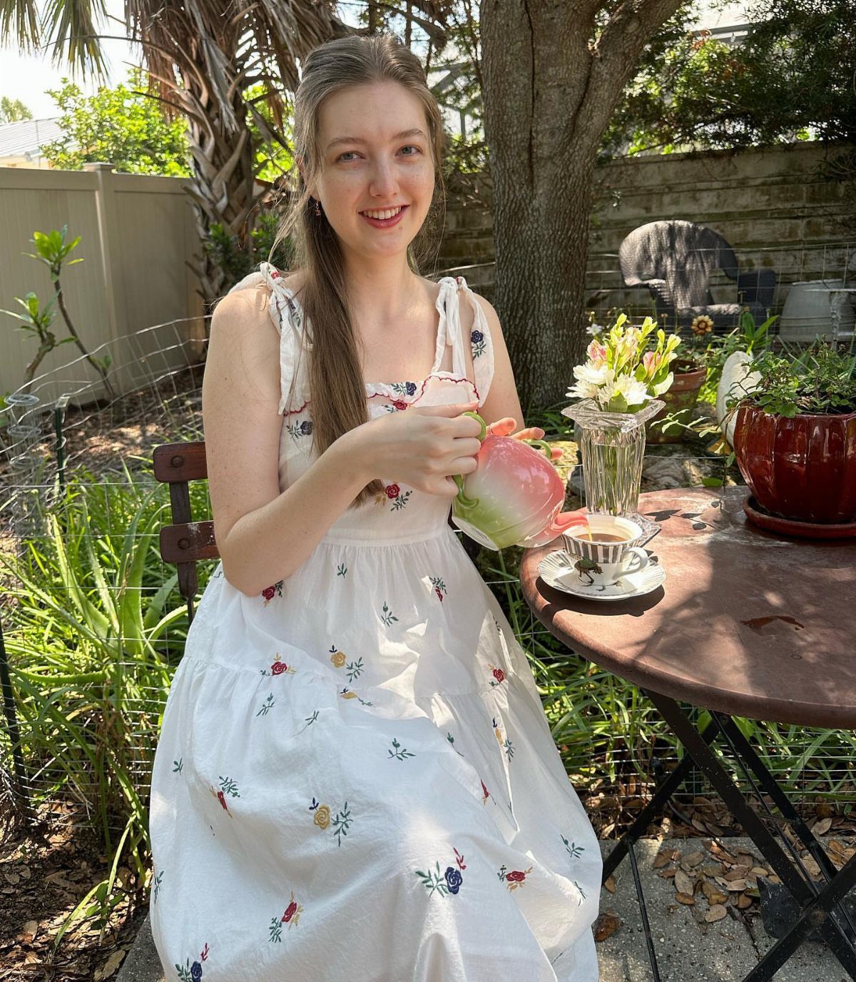 Woman in a white floral dress pouring tea at an outdoor garden table