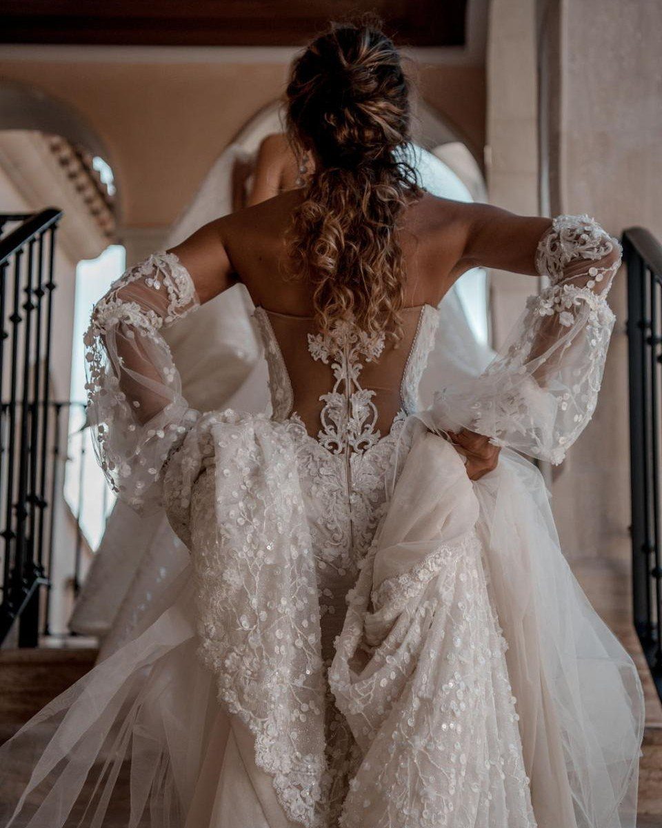 Woman from behind in a fitted lace wedding dress with sheer sleeves and tulle.
